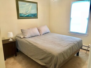 Relax in this serene bedroom with a large bed, framed sailboat painting, and natural light pouring in through the window.