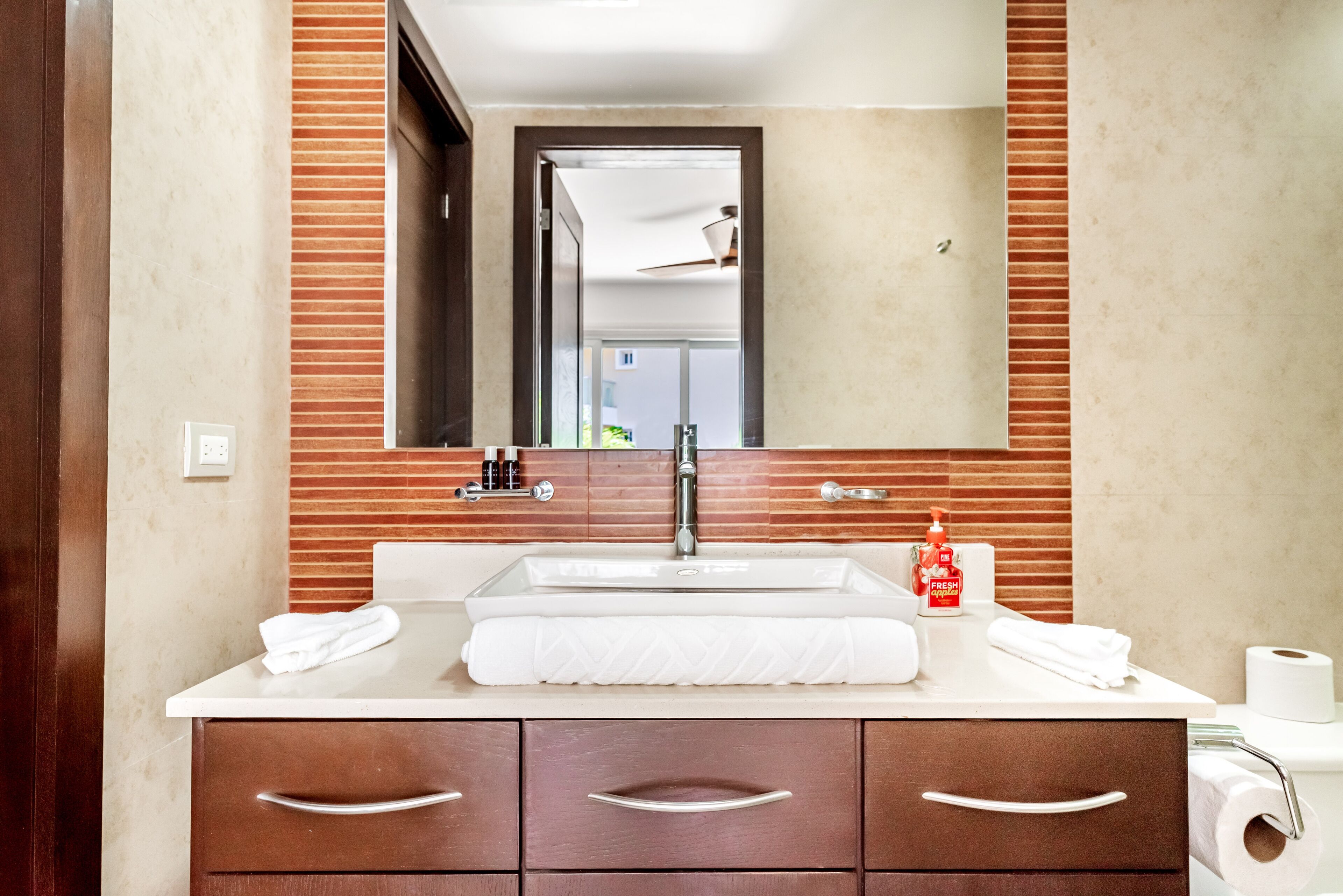 Un baño con lavamanos blanco, espejo y cómoda de madera con cajones.