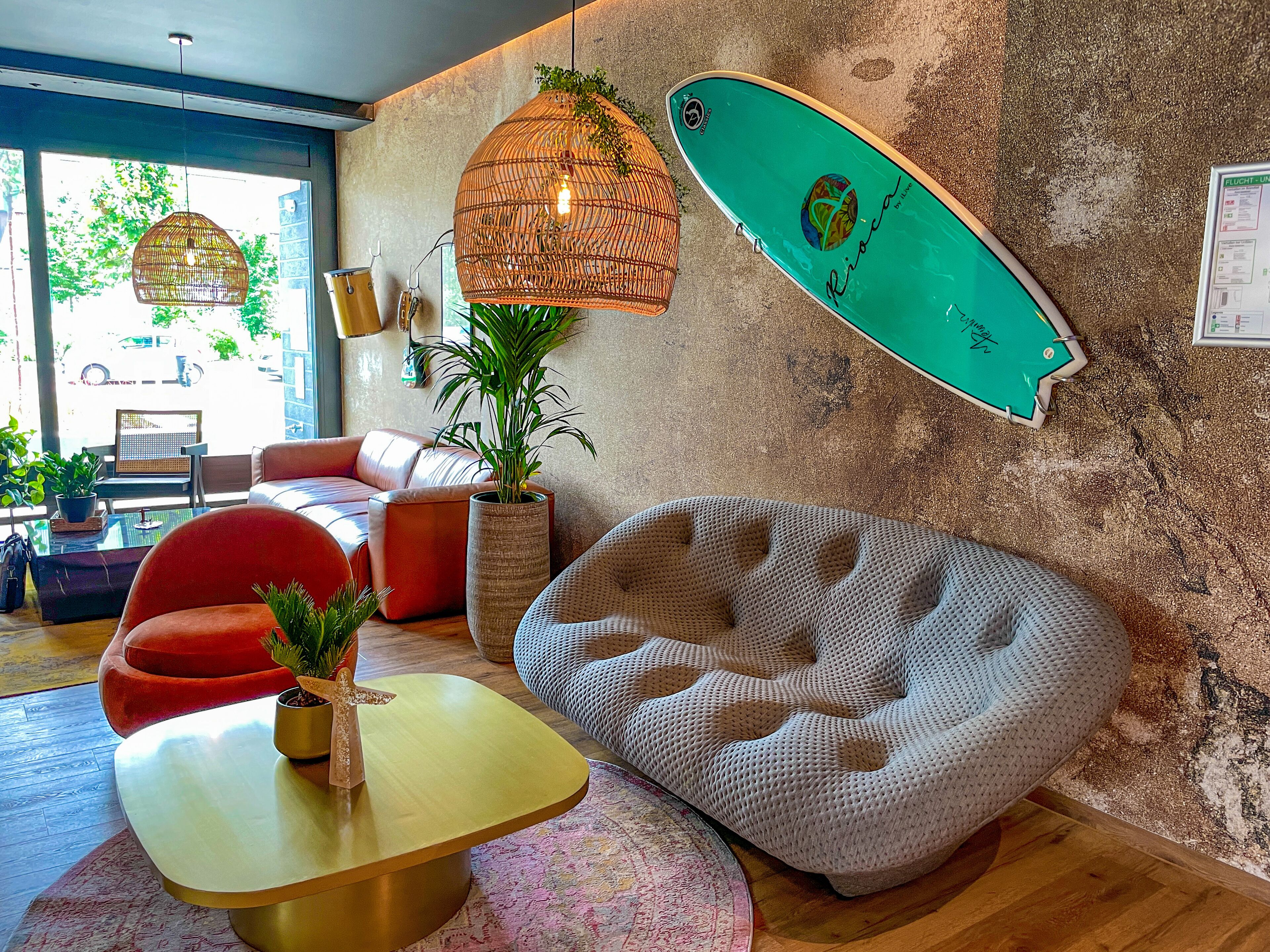 A modern lounge with a surfboard, wicker pendant lights, and a cozy seating area.