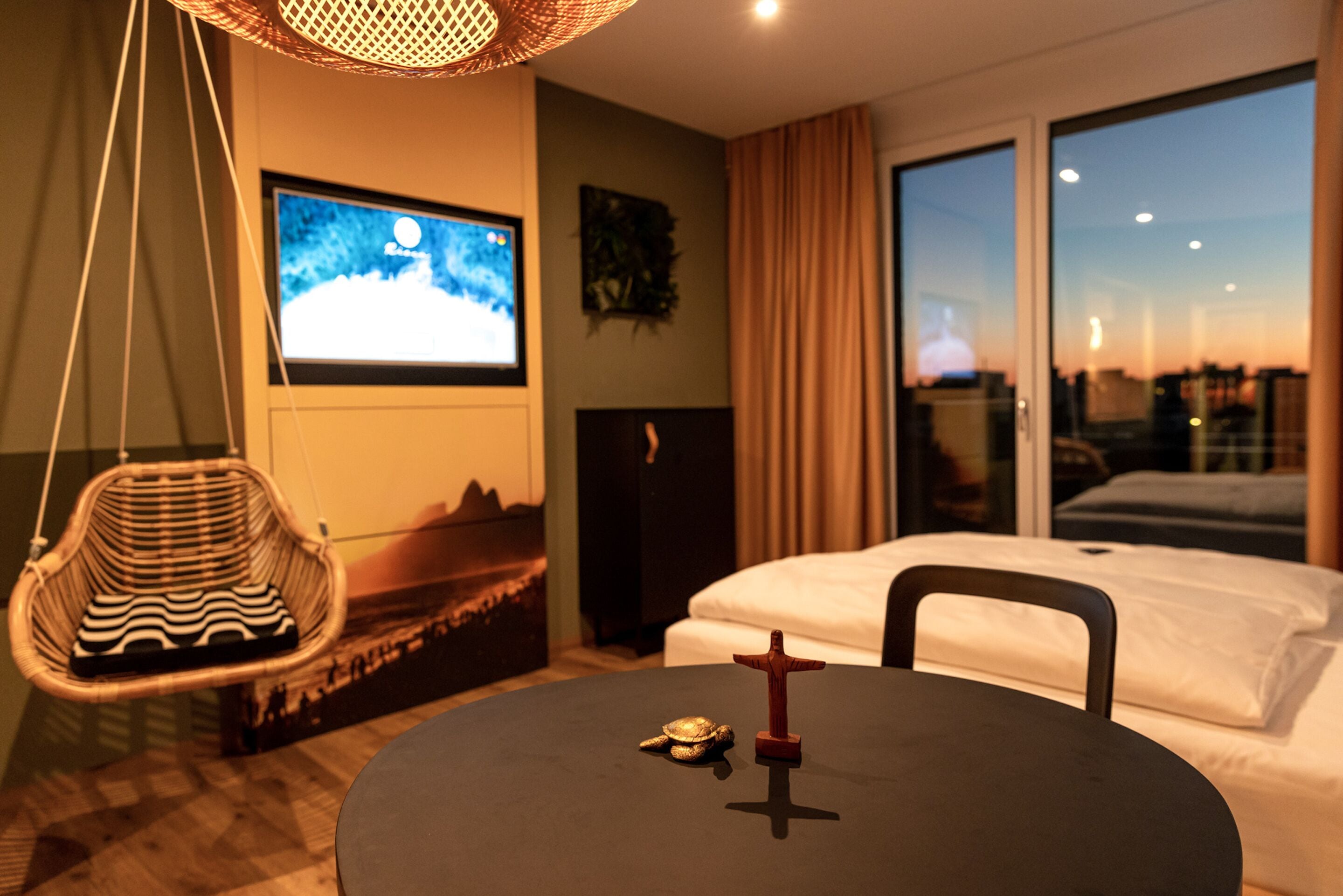 A modern hotel room with a bed, a television, a small table with a figurine, and a hanging chair.