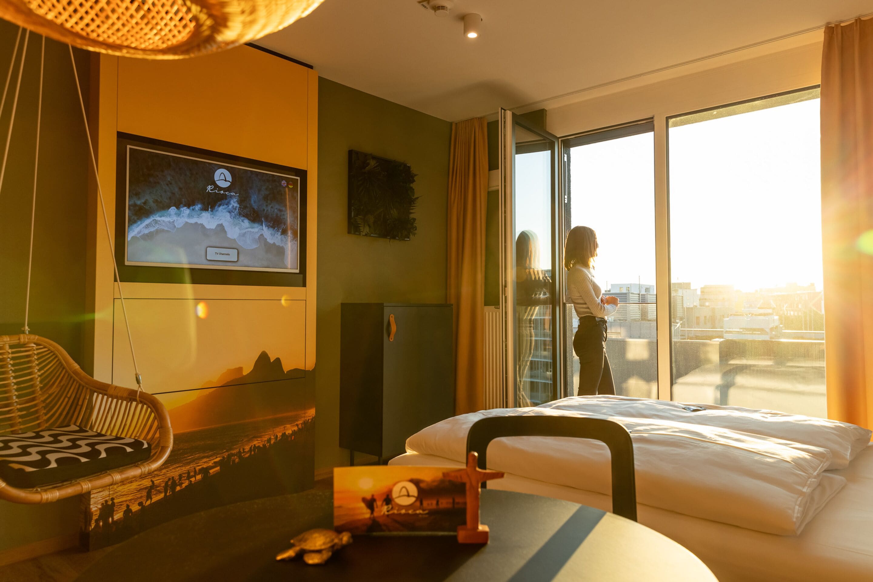 Hotellihuone, jossa on sänky, televisio, sohva ja ikkunasta avautuva näkymä kaupunkiin.
