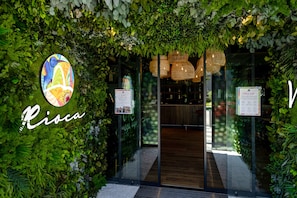 A restaurant entrance with a green leafy archway, a colorful logo, and a menu sign.