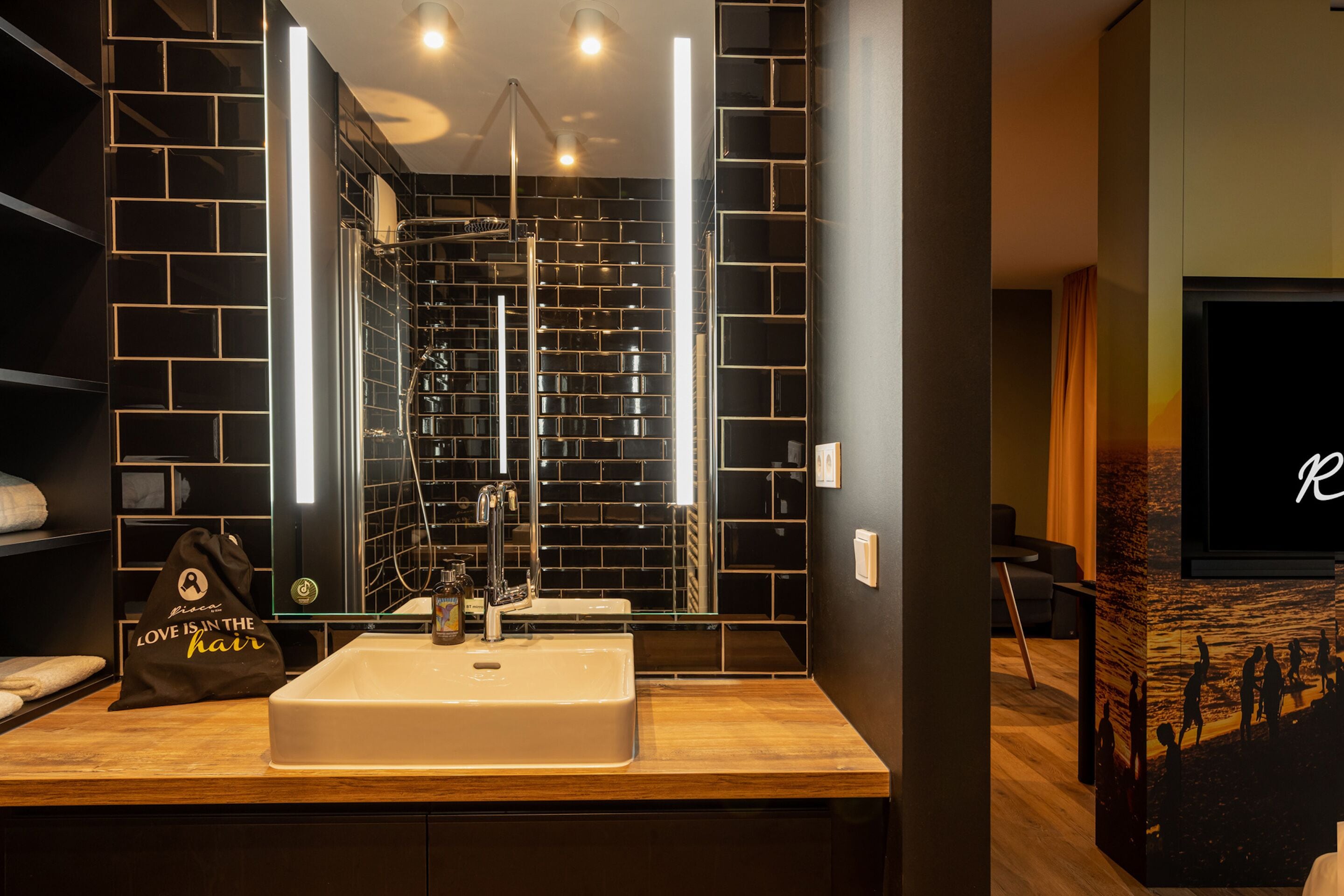 A modern bathroom with a large mirror, black tiled walls, and a wooden vanity.
