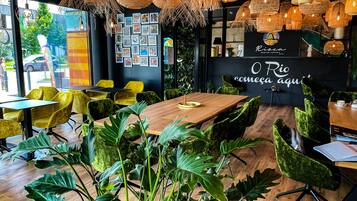 L’intérieur d’un restaurant moderne, avec une table à manger en bois, des chaises recouvertes d’un tissu vert et des lampes en osier suspendues au plafond.