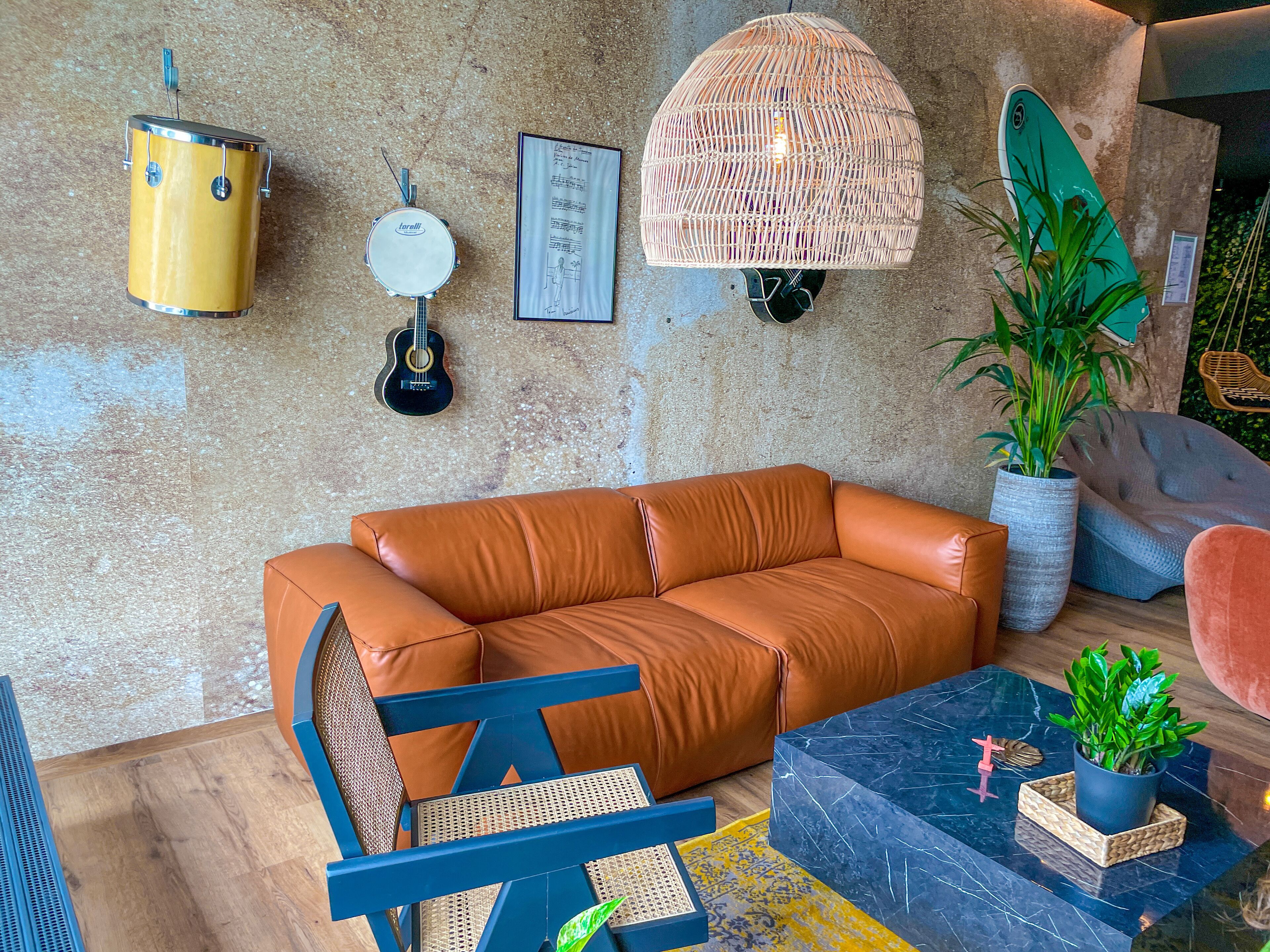 A modern living room with a leather sofa, a blue chair, a coffee table, and a hanging light fixture.