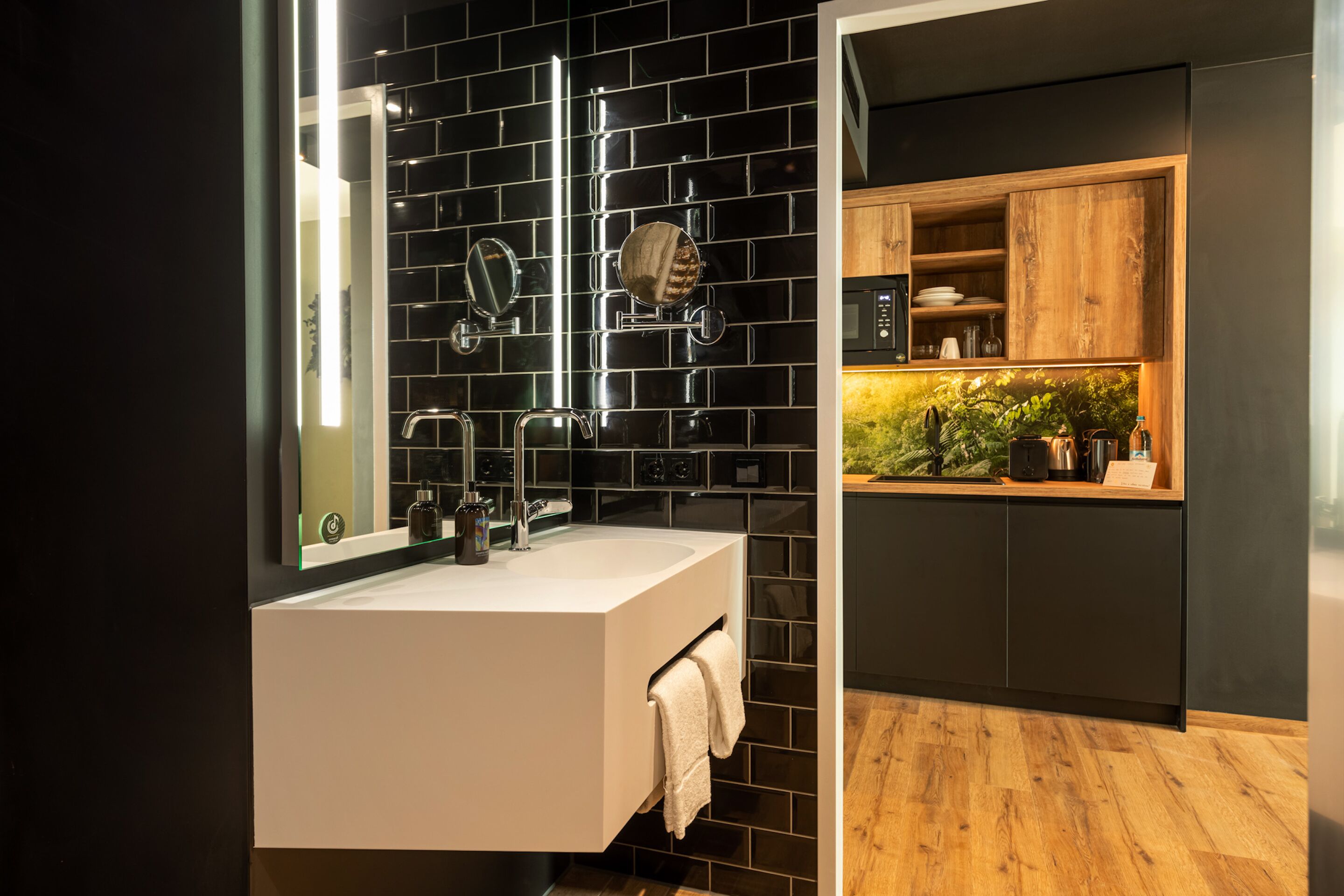 Ein modernes Badezimmer mit einem weißen Waschbecken, schwarzen Fliesenwänden und einem Holzboden.