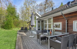 Une terrasse en bois avec des meubles d’extérieur, une table en verre et un barbecue.