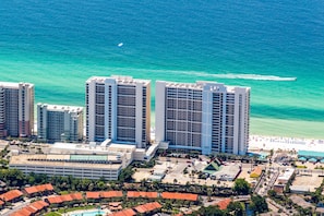 A high-rise hotel with multiple floors, a beach, and a parking area.