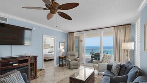 Un soggiorno spazioso con una grande TV a schermo piatto, una ventola a soffitto e vista sull'oceano attraverso le porte scorrevoli in vetro.