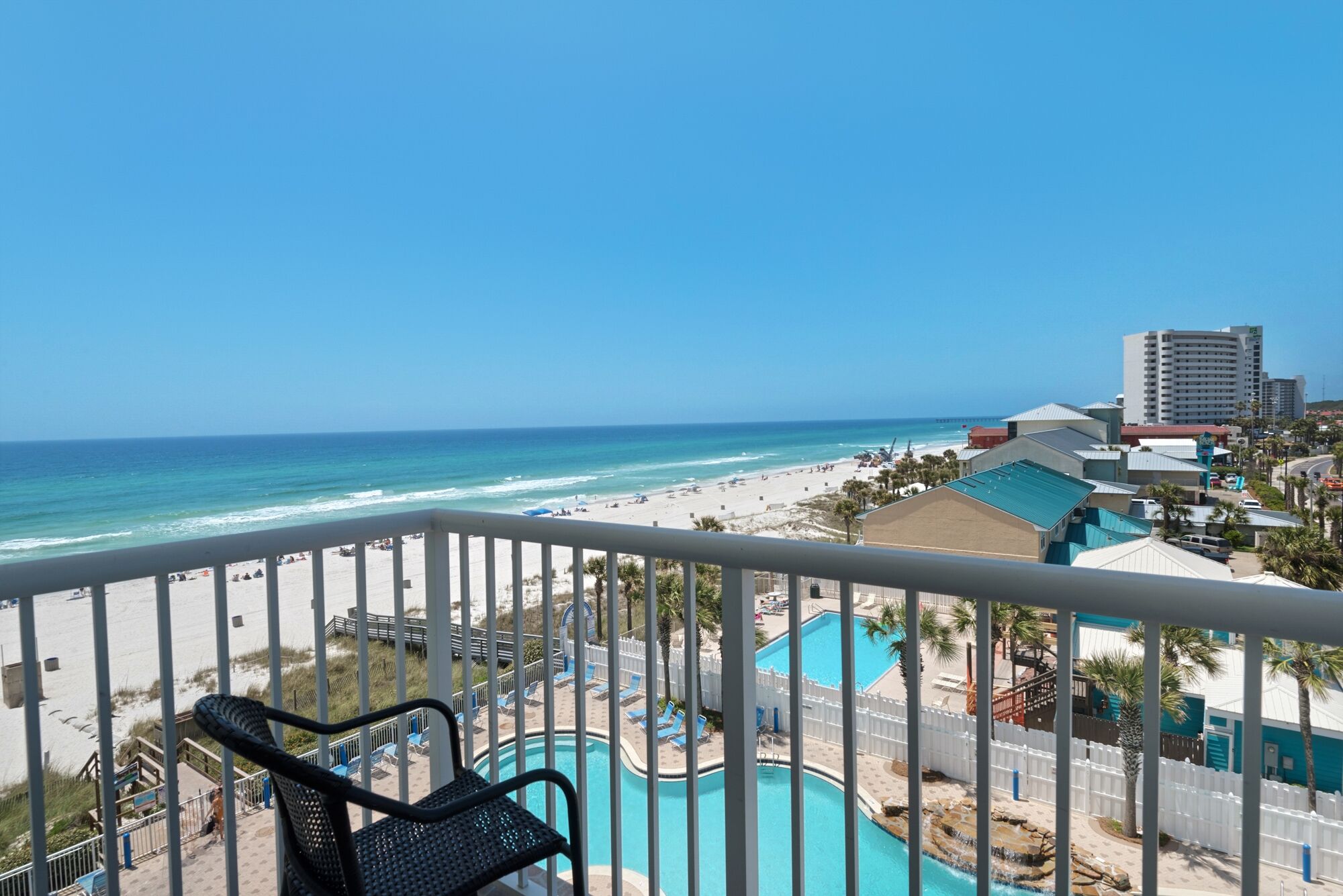 Ein Balkon mit Blick auf einen Strand, ein Schwimmbad und ein Hotelgebäude.