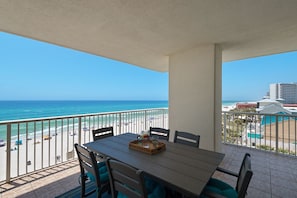 Un balcon avec une table et des chaises, donnant sur une plage et l’océan.