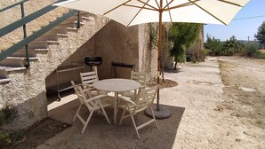 A rustic outdoor seating area with a round table and chairs, a large umbrella, and a staircase leading up to a building. - Casolare Fonte di Moro (Abruzzo)