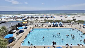Zona de piscina con vista a la playa, múltiples sombrillas y sillas de descanso.