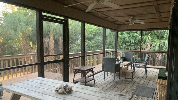Un espace extérieur abrité doté d’une terrasse en bois, d’une table avec un panier, de chaises en osier et d’un ventilateur de plafond.