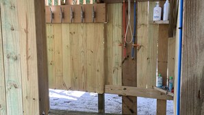 Une structure en bois dotée d’une porte en métal, d’un banc en bois et d’une étagère contenant des articles de toilette.