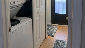 Une buanderie équipée d’un lave-linge et d’un sèche-linge à chargement frontal, d’un tapis gris et d’une porte donnant sur une pièce avec vue.