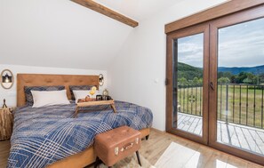 A bedroom with a large bed, a wooden headboard, a bench, and a balcony with a view of the countryside. - Pet friendly home in Gospic (Gospic)