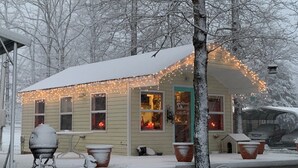 A house with a porch decorated with string lights, a visible gift shop sign, and snow-covered steps. - Water front cottage w/water access, firepit & great sunsets. (Vonore)