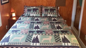 A bedroom with a wooden paneled wall, a quilted bedspread, a bedside table with a lamp, and a framed picture on the wall. - Water front cottage w/water access, firepit & great sunsets. (Vonore)