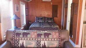 A cozy room with a brown leather sofa, a quilted bedspread with animal prints, a ceiling fan, and a wooden wall panel. - Water front cottage w/water access, firepit & great sunsets. (Vonore)