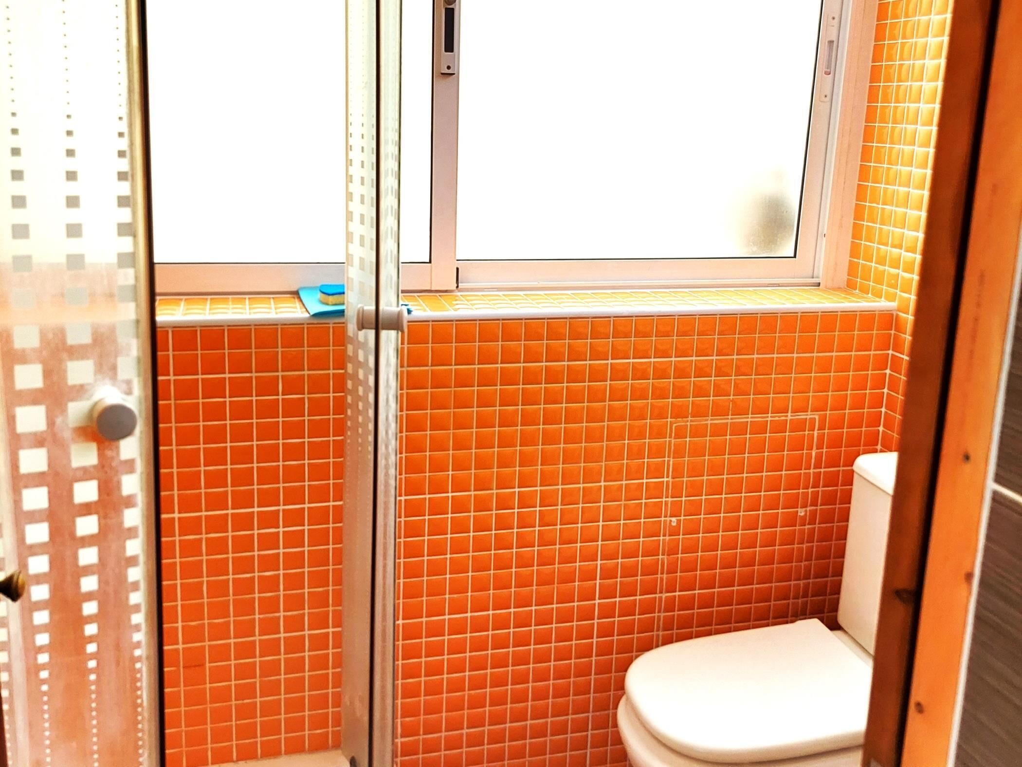A bathroom with orange tiled walls, a white toilet, and a glass shower enclosure.
