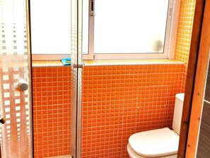 Un baño con paredes de azulejos naranjas, inodoro blanco y cabina de ducha de vidrio.