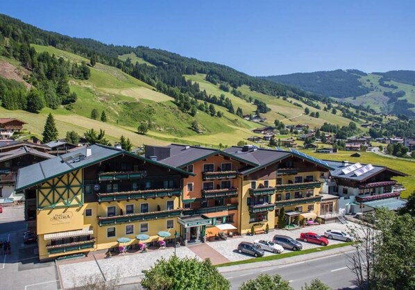 A hotel with multiple floors, outdoor seating, and a view of the surrounding hills. - Hotel Austria (Saalbach-Hinterglemm)