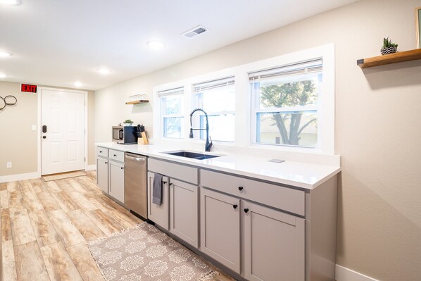 A kitchen with a white countertop, grey cabinets, a sink, and a window with blinds. - Magnolia Inn (Hermann)