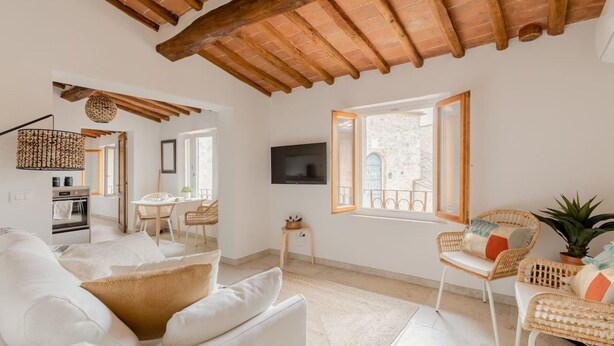A spacious living room with a high wooden ceiling, a dining area with wicker furniture, and a view of a stone building through a large window. - Stylish Luxury Loft Sleeps 4 San Gimignano Tuscany (San Gimignano)