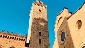 A historic stone tower with arched windows and a crenellated roof, adjacent to a building with a round window and a doorway. - Stylish Luxury Loft Sleeps 4 San Gimignano Tuscany (San Gimignano)