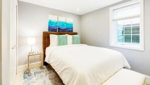 A bedroom with a bed, a nightstand, a painting, and a window. - Stylish Modern Suite in the Heart of Chevy Chase! (Washington)