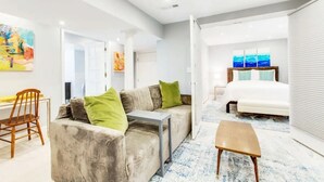 A modern hotel room with a grey sofa, a small table, and a bed with blue bedding. - Stylish Modern Suite in the Heart of Chevy Chase! (Washington)