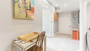 A hallway with a dining area featuring a wooden table and chairs, a large abstract painting, and a door leading to another room. - Stylish Modern Suite in the Heart of Chevy Chase! (Washington)