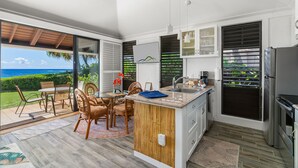 Una cocina moderna con una isla grande, un comedor con sillas de mimbre y vista al océano.