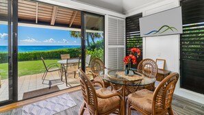 Un comedor con mesa de vidrio y sillas de mimbre, con vistas a un jardín exuberante y el océano.