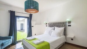 Una camera da letto con un letto, una poltrona blu, una copriletto verde e un lampadario.
