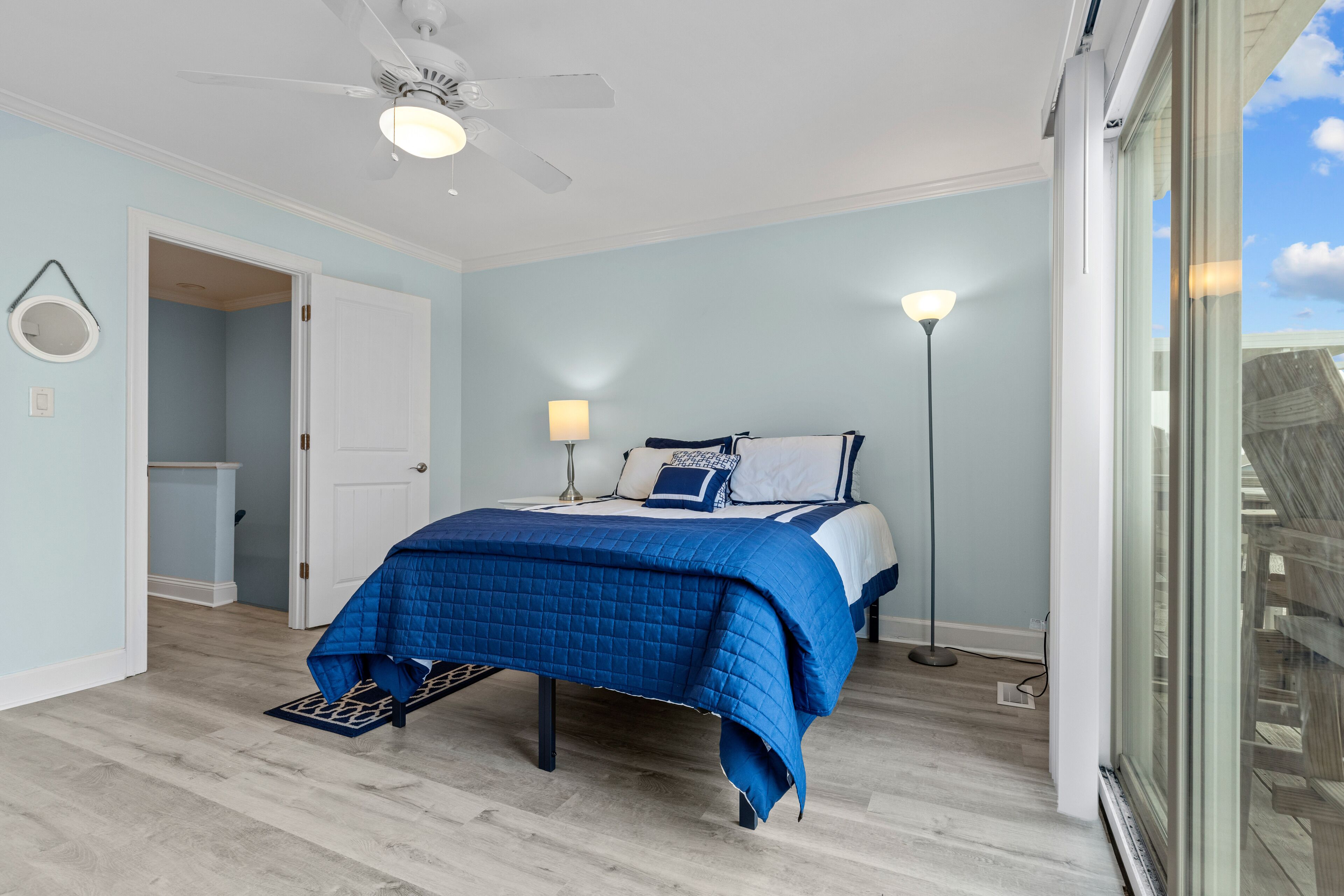 Een slaapkamer met een bed, een plafondventilator, een vloerlamp en uitzicht op het omliggende landschap.