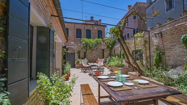 A narrow courtyard with a wooden table set for dining, surrounded by brick walls and potted plants. - Ca' Minore Secret Garden (Venice)