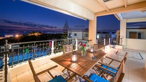 A terrace with a wooden table and chairs, a railing, and a view of the city at dusk. - Palaiochora Retreat - Sea Sunset Rooftop (Avia Kalamata)