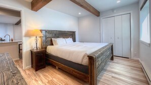 A bedroom with a wooden bed frame, a bedside table with a lamp, a wardrobe, and a view of the bathroom.