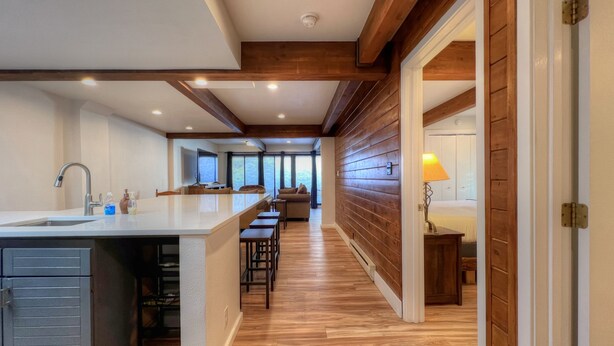 A modern kitchen with a central island, wooden flooring, and a view of the living area.