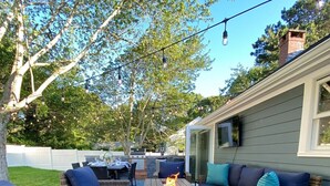 Eine Terrasse im Freien mit Korbmöbeln, einem Feuerkorb und Lichterketten.