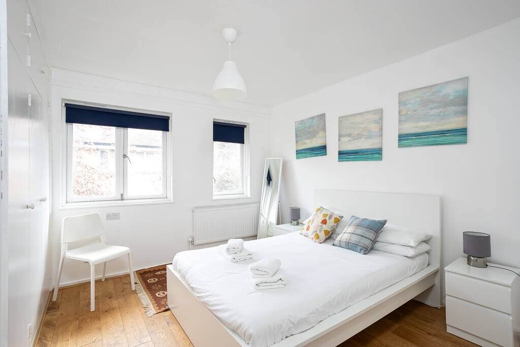 A bedroom with a bed, a chair, a bedside table, a lamp, and artwork on the wall.