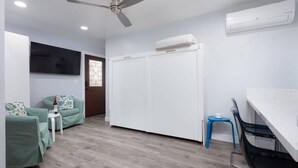 A room with a ceiling fan, a white wardrobe, a dining table with chairs, and a green sofa with a small table. - Charming Private Mission Bay Studio 2 (San Diego)