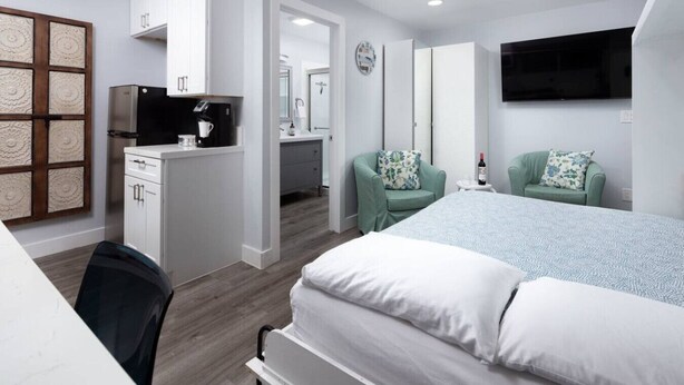 A modern hotel room with a bed, desk, chairs, and a TV. - Charming Private Mission Bay Studio 2 (San Diego)