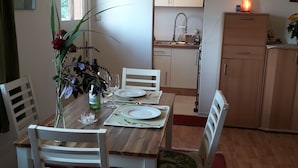 Ein Essbereich mit einem Holztisch für vier Personen, weißen Stühlen, einer Blumenvase und einer Küche im Hintergrund.