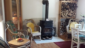 Ein gemütliches Wohnzimmer mit Korbmöbeln, einem Kaminofen und einem Esstisch.