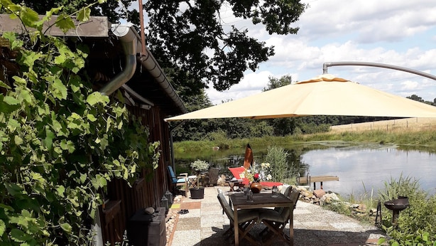 Eine Terrasse mit Tisch und Stühlen, ein kleiner Tisch mit Blumen und ein Teich im Hintergrund.