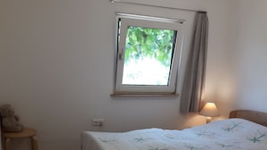 Ein Schlafzimmer mit einem Bett, einem Fenster, einem Nachttisch, einer Lampe und einem Teppich.