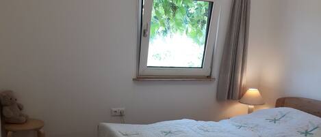 Un dormitorio con cama, ventana, mesita de noche, lámpara y alfombra.